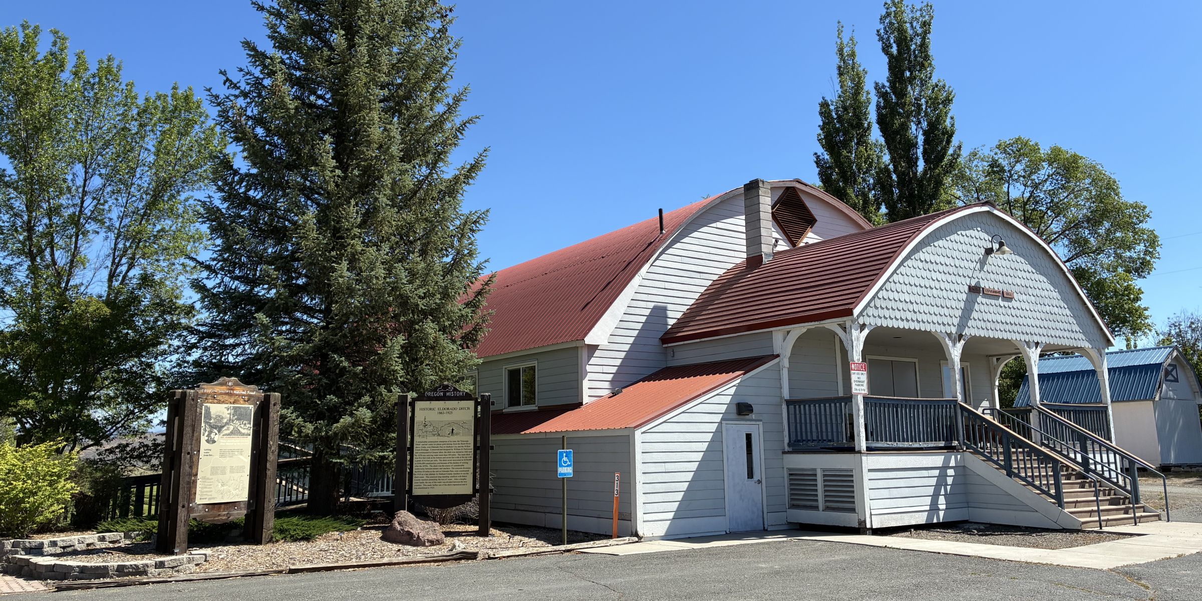 Two wooden signs next to white community center building. Blue sky and green tree background. 