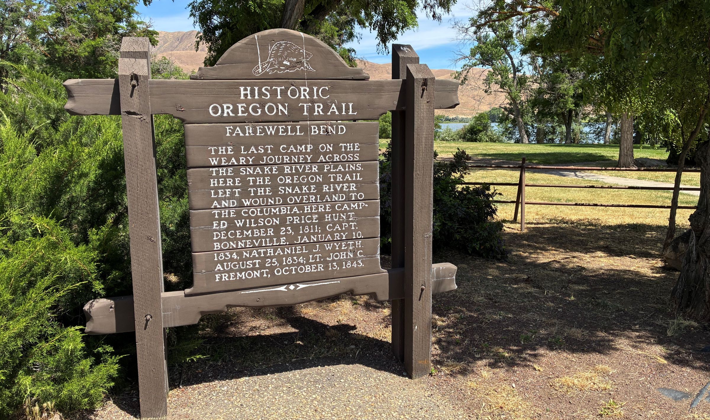 Old wooden sign with green grass, brown hills, and blue sky in background. 