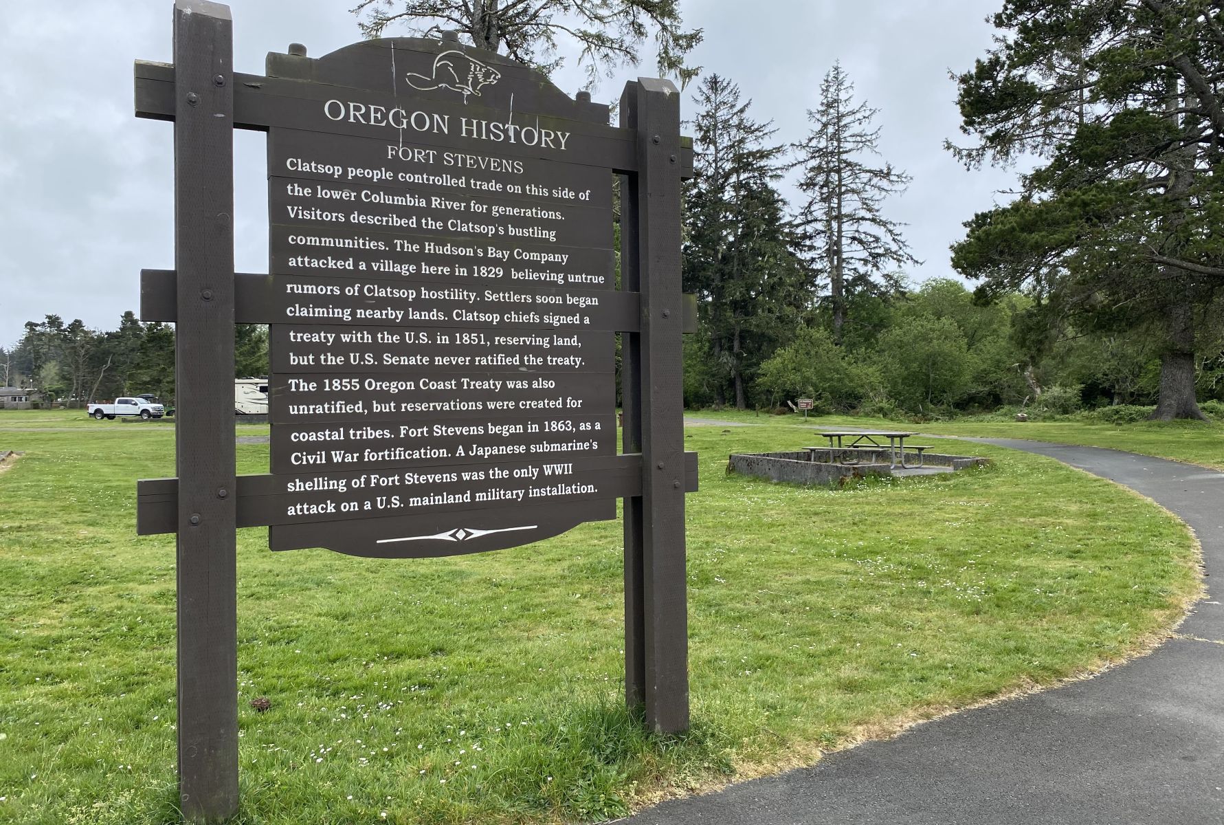 Image of brown routed historical marker on left of paved walkway. Sign is routed with white letters and beaver at top.