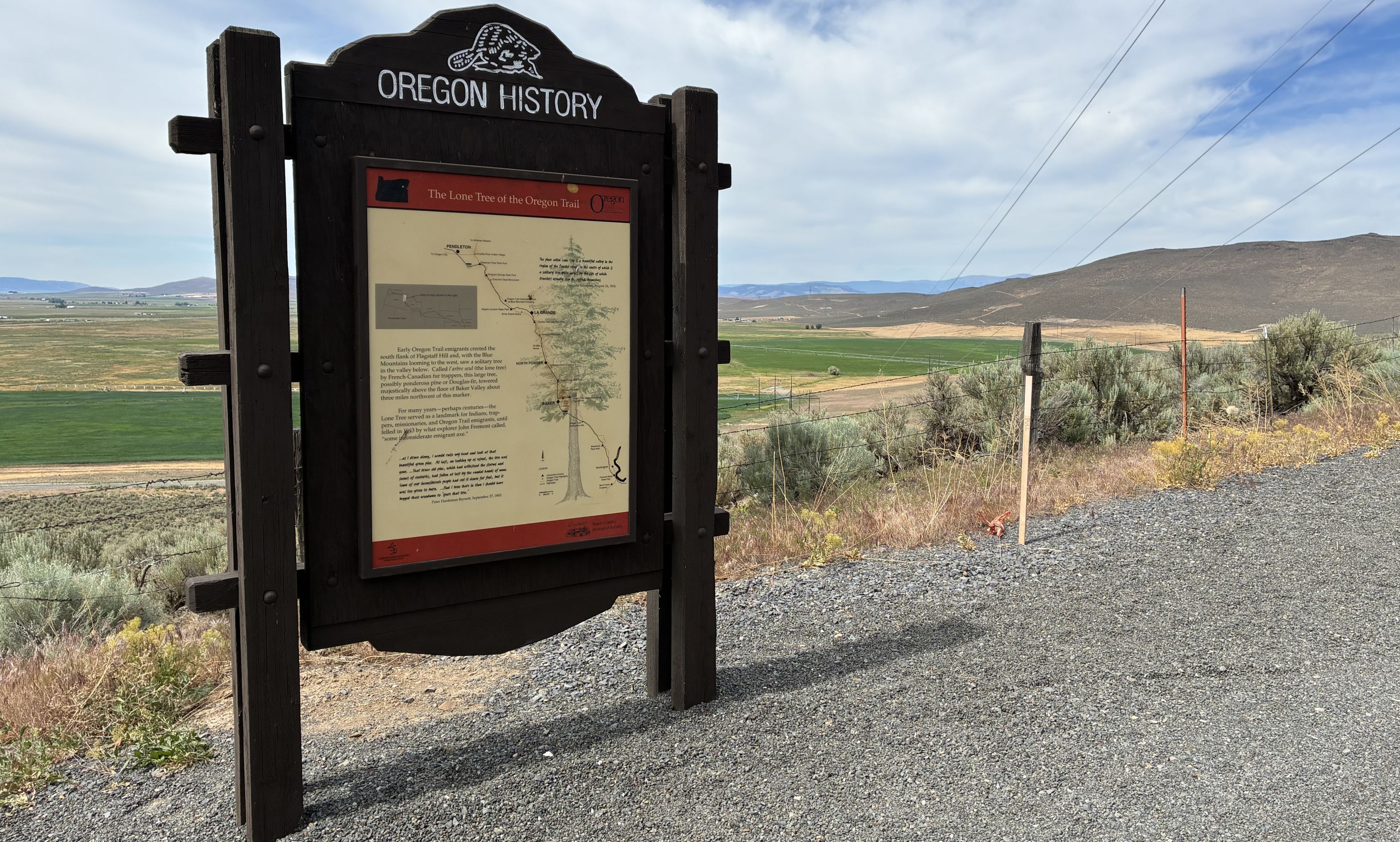 Wooden sign on gravel road with view of valley in background. 