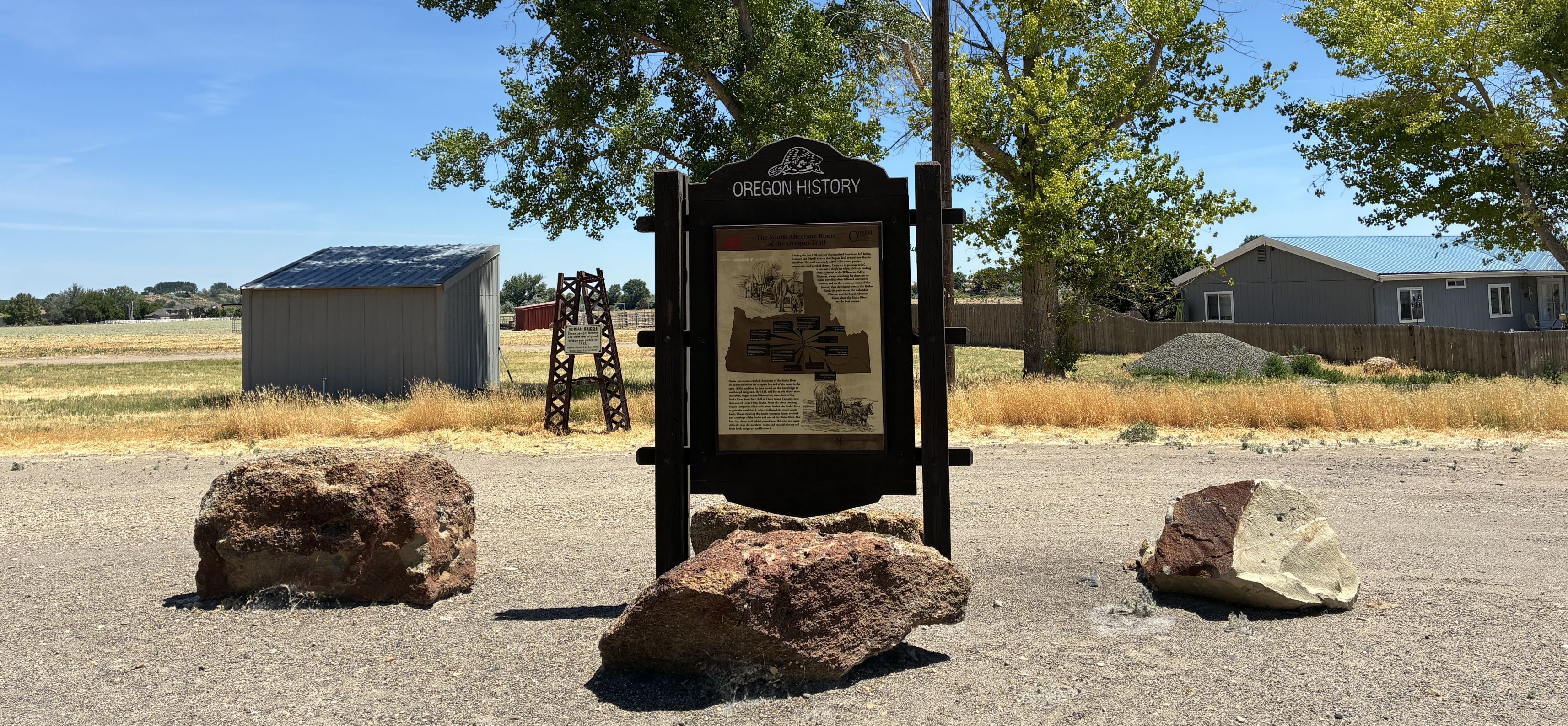 Wooden sign with boulders in foreground, blue sky and house in background.